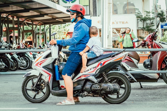 Muž s dieťaťom na motorke v meste